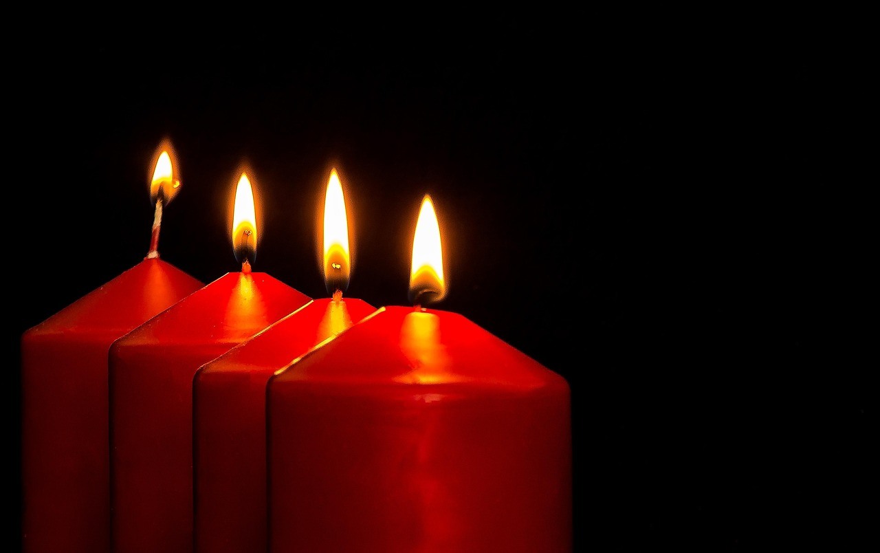 Four red square pillar candles stand against black, each showing a bright flame and sloping top.