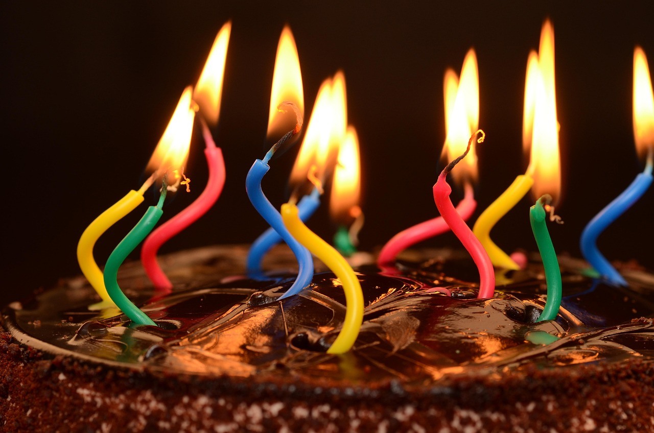 Curled multicolored candles burn on a chocolate cake covered with textured shavings.